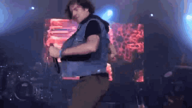 a man in a denim vest is singing into a microphone on a stage