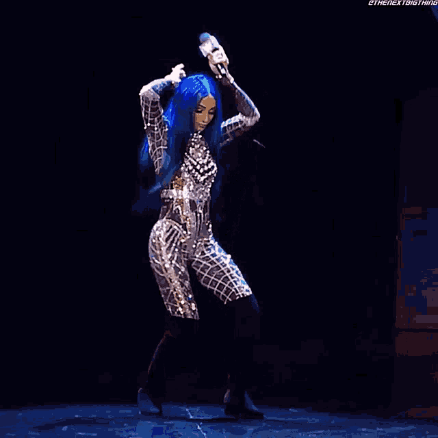 a woman with blue hair is holding a microphone in her hands while dancing on a stage .