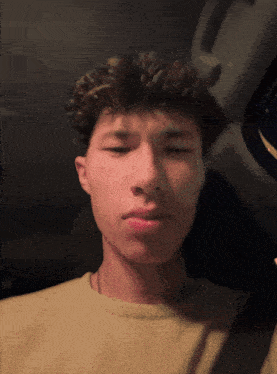 a man with curly hair is wearing a tan shirt