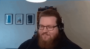 a man with a beard and glasses is wearing headphones and smiling .