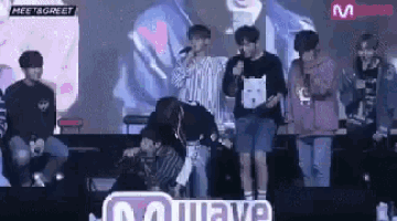 a group of young men are standing on a stage holding microphones and singing into them .