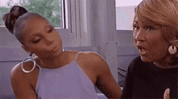 two women are sitting next to each other in front of a window .