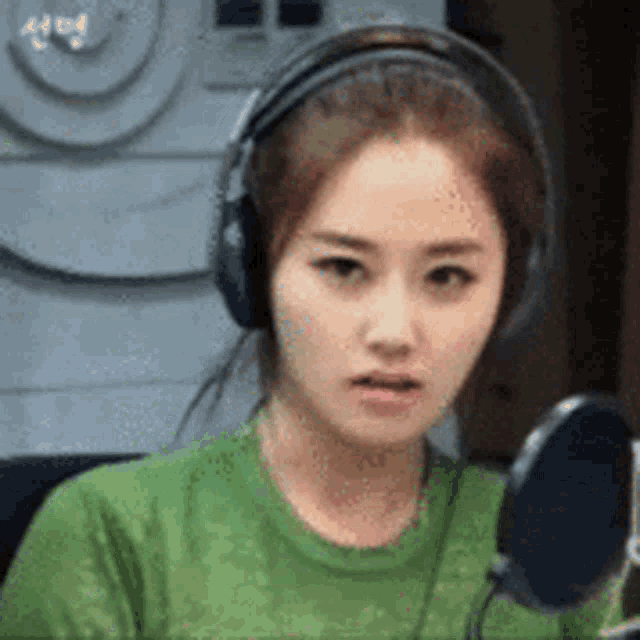 a woman wearing headphones and a green shirt is looking at the camera .