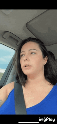 a woman in a blue tank top is sitting in a car with a seat belt around her neck .