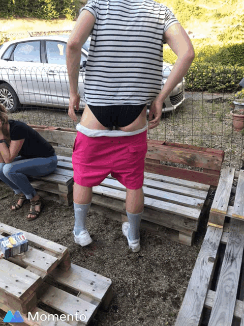 a man wearing pink shorts and a striped shirt is standing on a wooden pallet