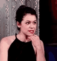 a woman in a black dress is sitting in front of a curtain .