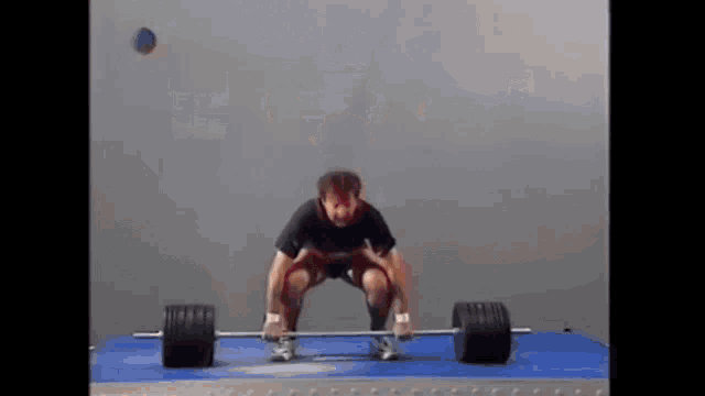 a man is squatting down to lift a barbell on a mat
