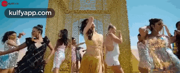 a group of women are dancing in front of a gold wall in a video .
