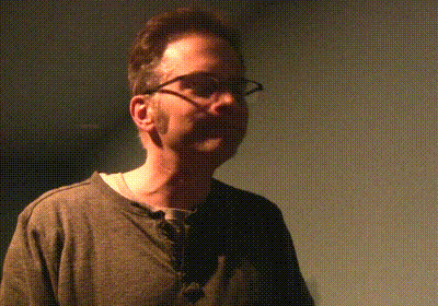 a man wearing glasses and a grey shirt is standing in a dark room
