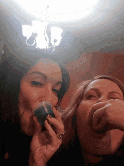 two women drinking from plastic cups in front of a light