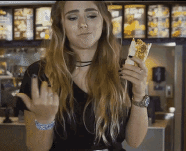 a woman in a black shirt is eating a burrito and giving the middle finger