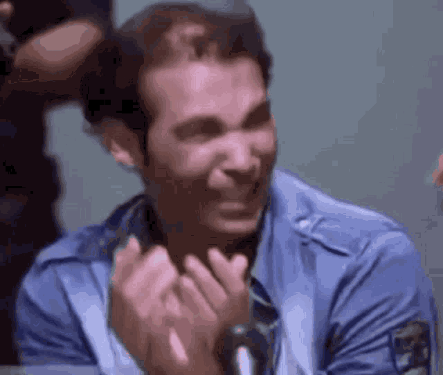 a man in a blue shirt is laughing and clapping his hands .