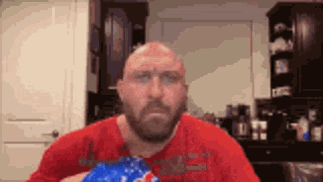 a bald man with a beard is holding a bag of popcorn in a kitchen .