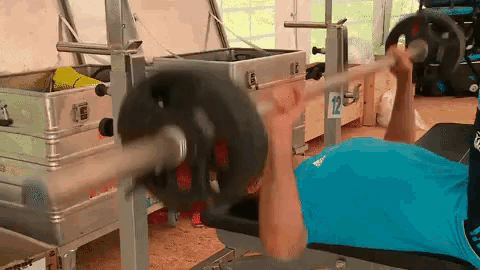 a man in a blue shirt is lifting a barbell in a gym