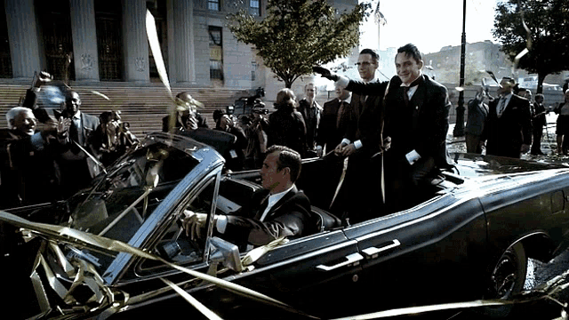 a man in a tuxedo is driving a car with gold ribbons around it