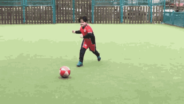 a girl in a red shirt is kicking a soccer ball on a field .