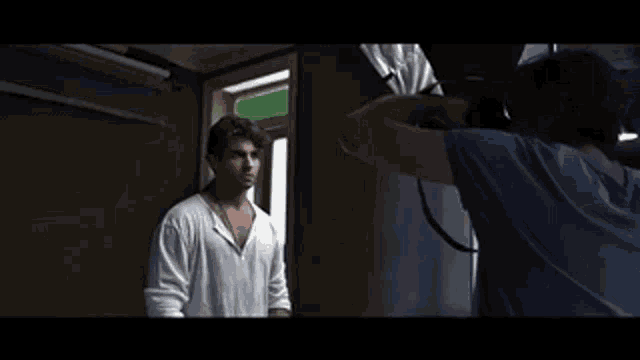 a man in a white shirt is being photographed by a cameraman in a dark room .