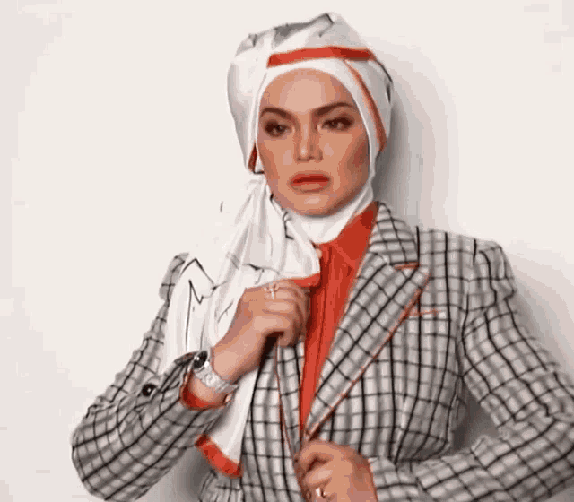 a woman wearing a hijab and a plaid jacket adjusts her jacket