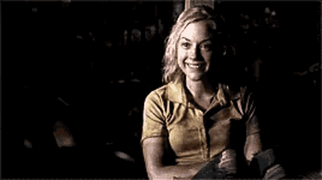 a woman in a yellow shirt is smiling in the dark while sitting on a bench .