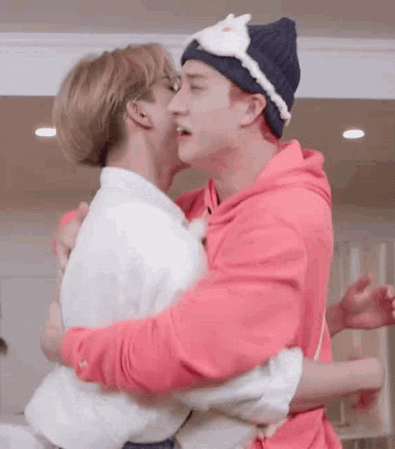a couple of men hugging each other in a room . one of the men is wearing a hat .