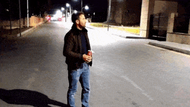 a man in a brown jacket is standing on a street holding a coke can