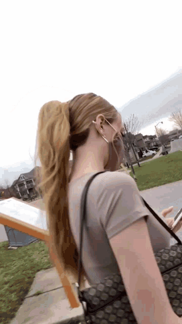 a woman wearing a mask and a ponytail holds a cell phone