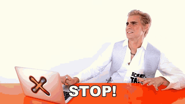 a man sitting at a desk with a laptop and a sign that says stop on it