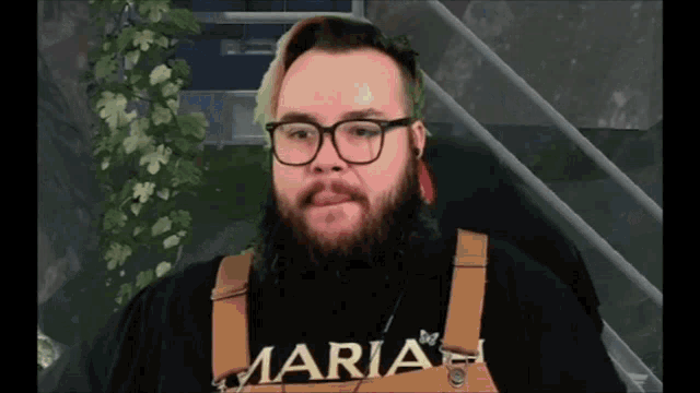 a man wearing glasses and overalls with the word maria on his chest