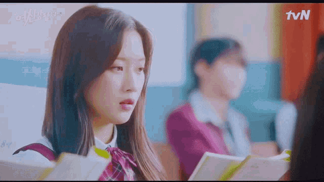 a girl in a school uniform is sitting in a classroom looking at a book .