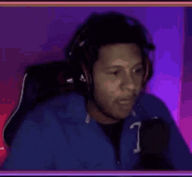 a man wearing headphones and a blue jacket is sitting in front of a microphone .