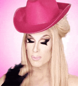a drag queen wearing a pink cowboy hat and black gloves on a pink background .
