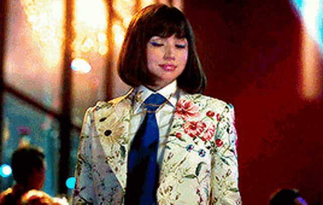 a woman wearing a floral suit and tie is standing in front of a crowd .