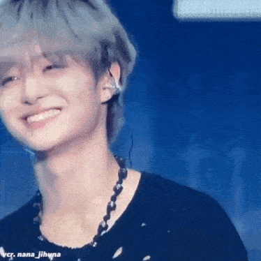 a close up of a person wearing a black shirt and a necklace smiling on a stage .