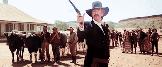 a man in a cowboy hat holds a gun in front of a herd of cows