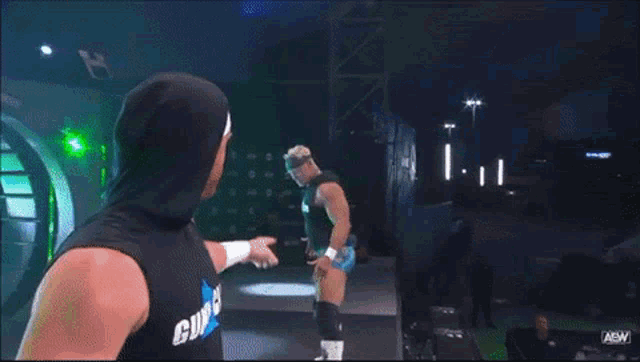 a man in a tank top that says gunn club shakes hands with another wrestler