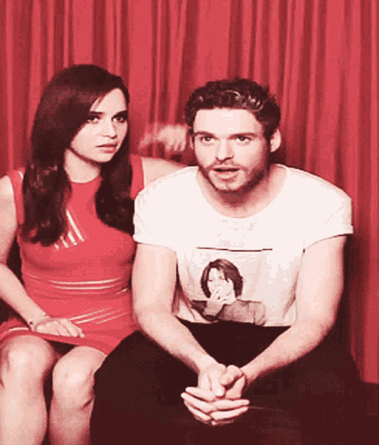a man and a woman sitting next to each other with a red curtain behind them