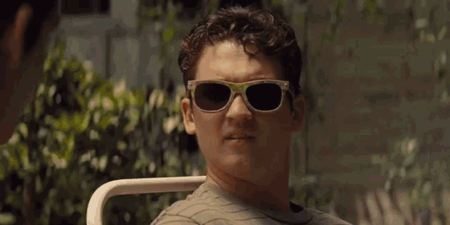 a man wearing sunglasses is holding an orange in his hand .