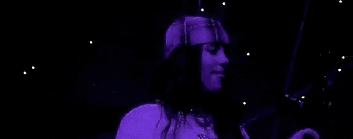 a woman is singing into a microphone while wearing a purple shirt and a hat .