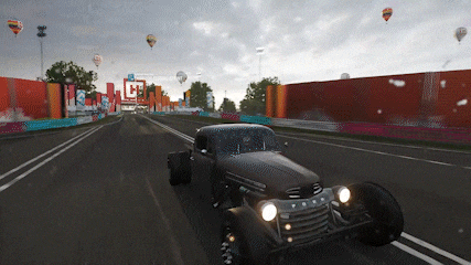 a car is driving down a road with hot air balloons flying in the sky