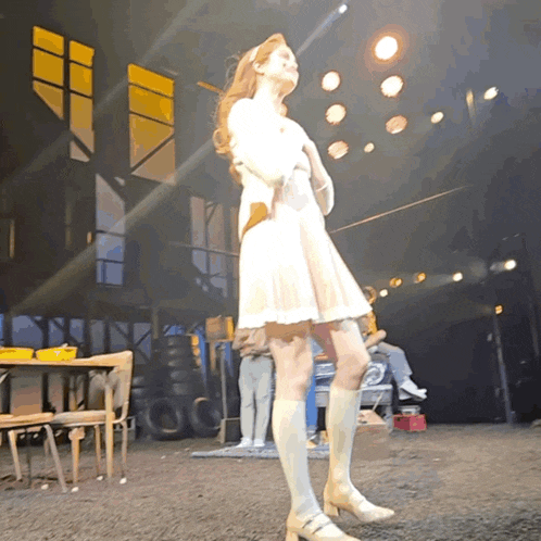 a woman in a white dress and white knee high socks stands on a stage