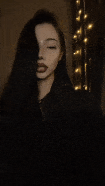 a woman with dark hair and red lipstick is smiling in front of a string of lights