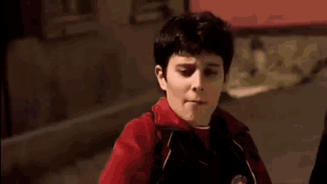a young boy in a red hoodie is standing in front of a building .