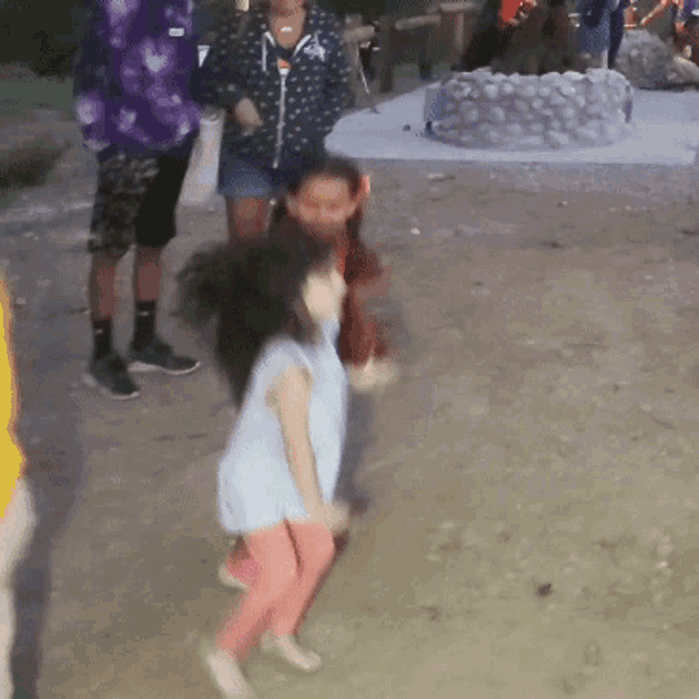 a little girl in a blue shirt and pink pants is dancing in the dirt
