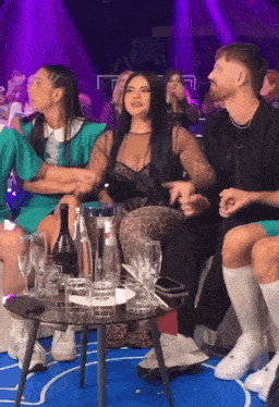 a group of people are sitting around a table with glasses and a bottle of wine