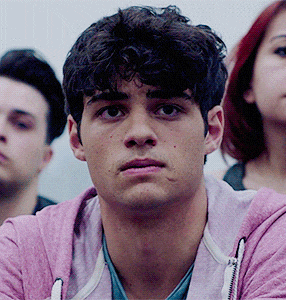 a man with curly hair wearing a pink hoodie looks at the camera