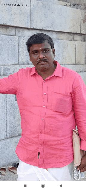 a man wearing a pink shirt is standing in front of a brick wall