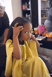 a little girl in a yellow dress is sitting in a chair getting her hair done .