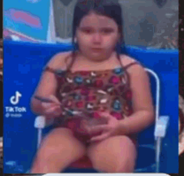 a little girl in a bathing suit is sitting in a chair holding a spoon and a bowl .
