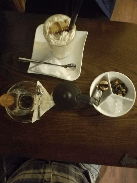 a table with a cup of cappuccino and a bowl of nuts