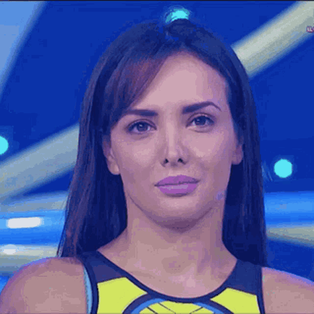 a woman wearing a yellow and black tank top is looking at the camera with a serious look on her face .